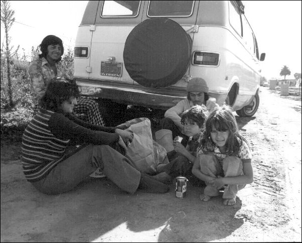 A migrant worker family eating in the shade of their van